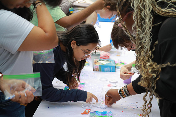 Group of UToledo students standing over a table working on a bead craft together