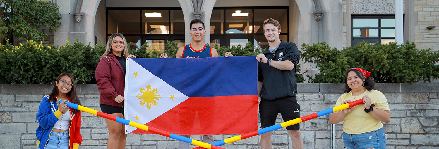 Filipino-American students posing with the Phlipino flag and tinkling dance sticks