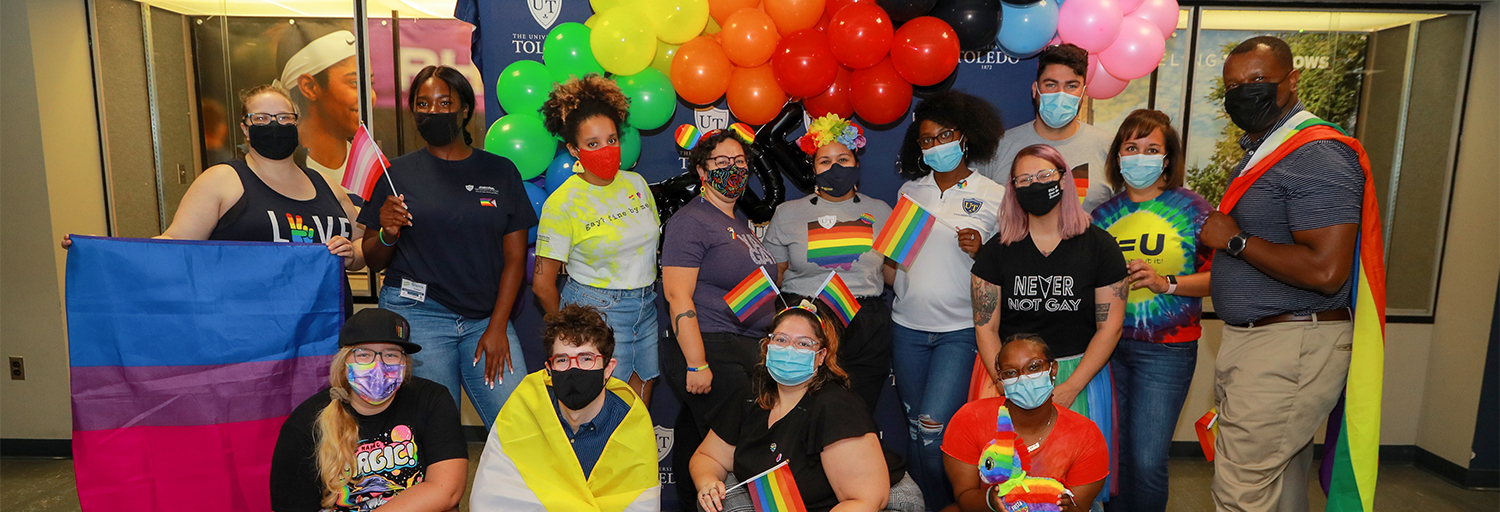LGBTQA+ students posing for camera in Trimble Lounge with flags and colorful balloons 