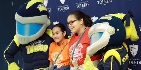 Two girls posing with Rocky and Rocksy at the Latino Youth Summit