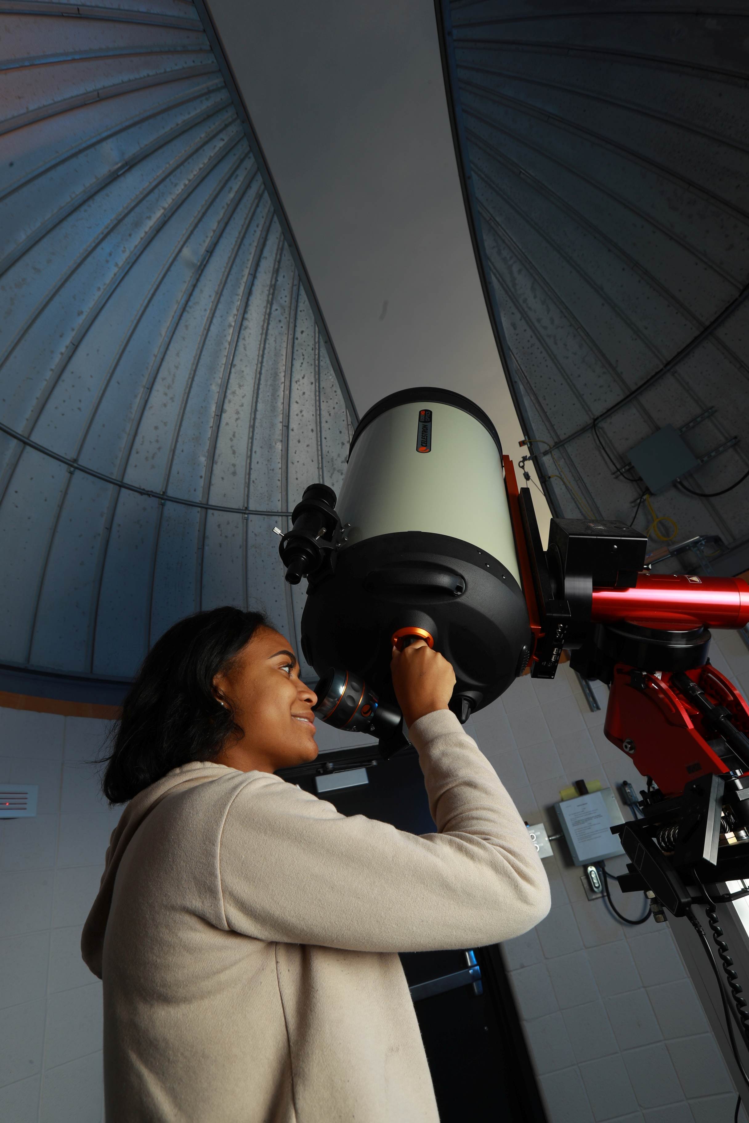 image of a young woman standing and looking through a telescope directed at the evening sky