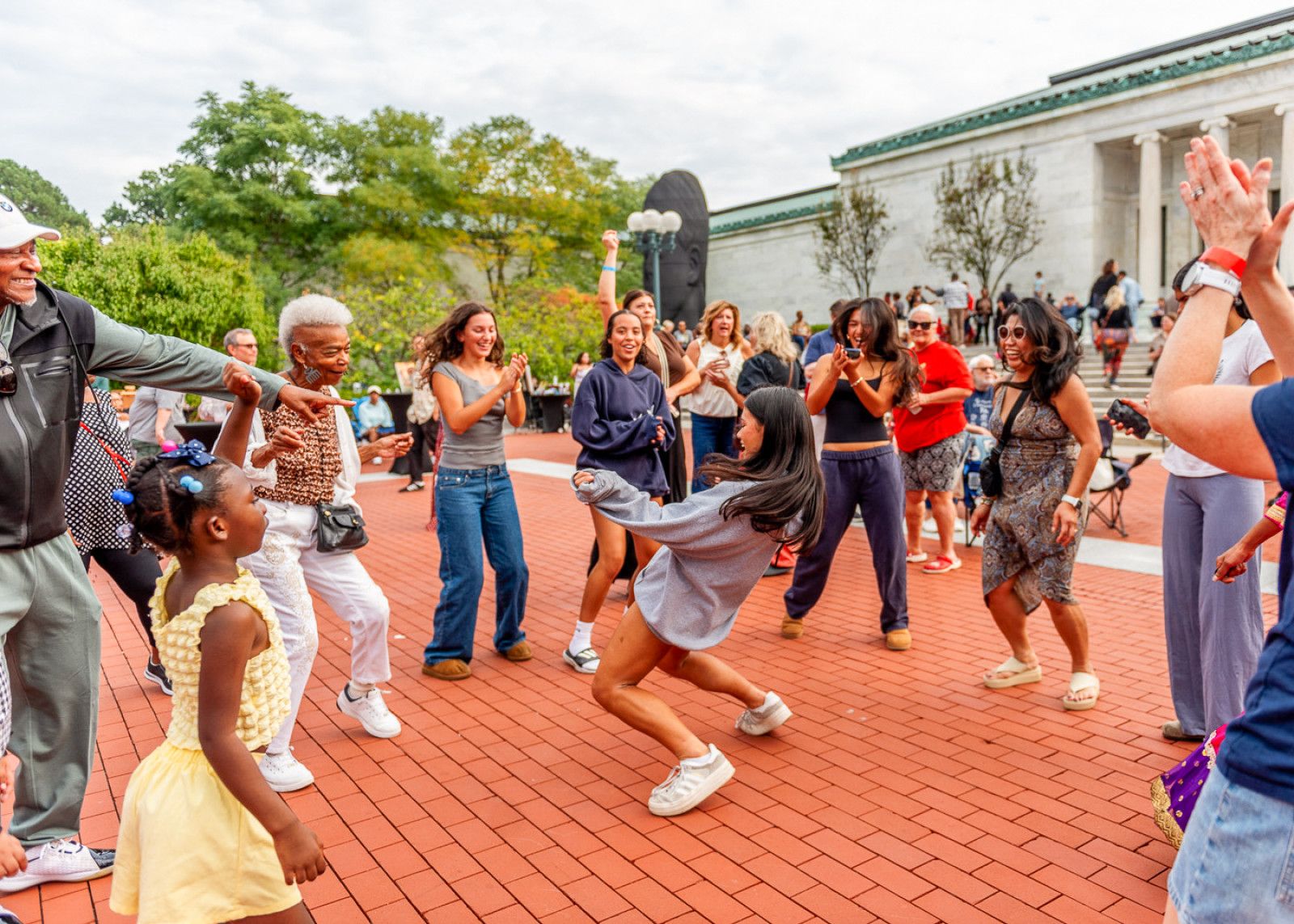 a crowd of individuals dancing in a circle outside of the Toledo Museum of Art