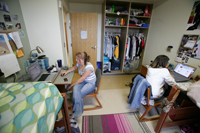 Two young women in their dorm room, sitting with their backs to each other, each at their desk and working on their computers.