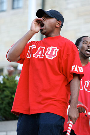 A student in a red shirt with Greek letters is shouting at an outdoor campus event.