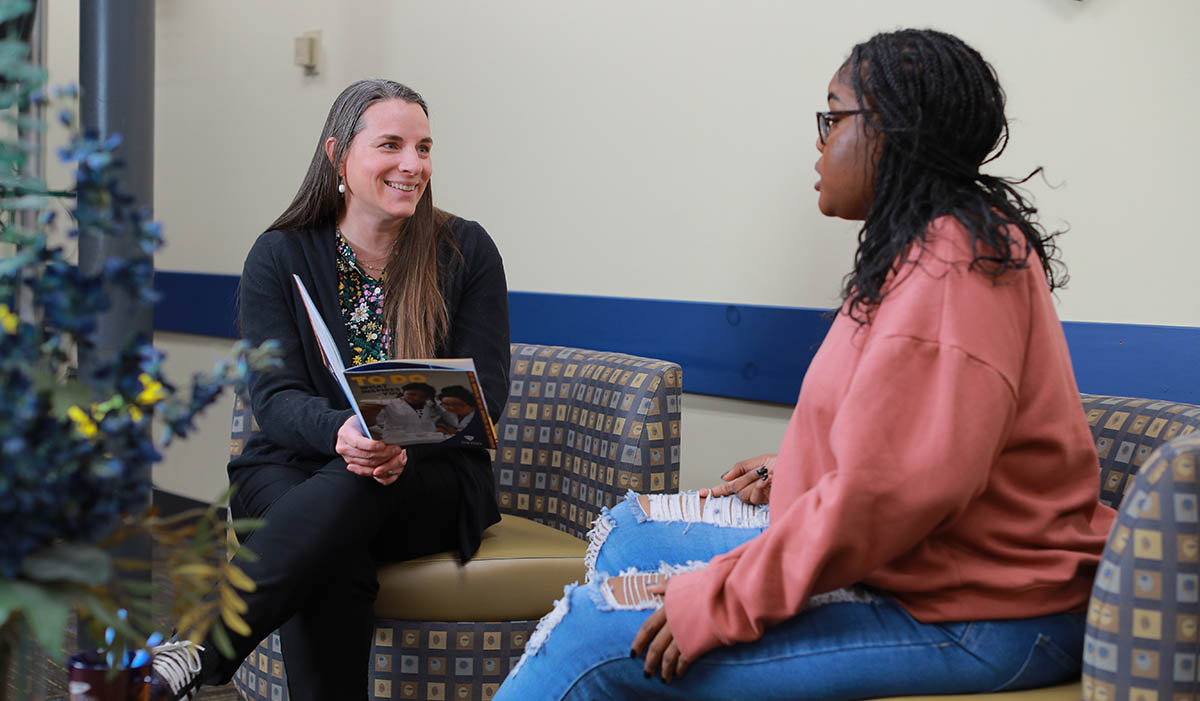 An academic counselor and student sitting on a couch talking