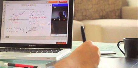 Laptop computer on a desk with a individuals hand writing with a pen