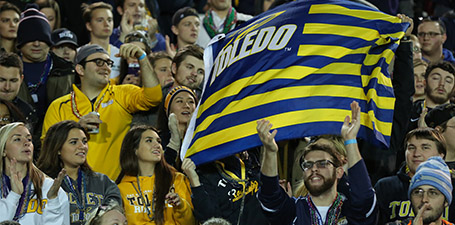 UToledo students in a crowd wearing blue and gold and waving a blue and gold flag