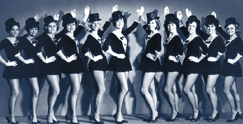 A black and white photo of a group of women lined up in dancing uniforms